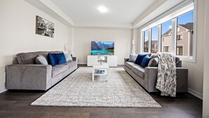Un salon moderne avec deux canapés gris, une table basse blanche et un grand téléviseur à écran plat.