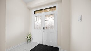 Une porte blanche avec des panneaux en verre dépoli, un paillasson noir et un petit vase contenant des fleurs blanches, posé sur le sol.