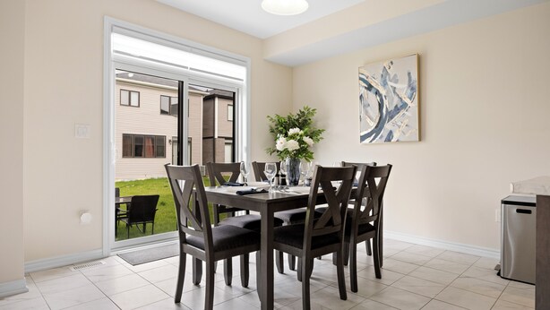 Un coin repas avec une table dressée pour quatre personnes, entourée de chaises en bois foncé, d’un vase rempli de fleurs et d’un tableau accroché au mur.