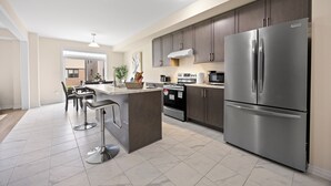 Une cuisine moderne dotée d’un îlot central, d’appareils électroménagers en acier inoxydable et de meubles de rangement aux couleurs sombres.
