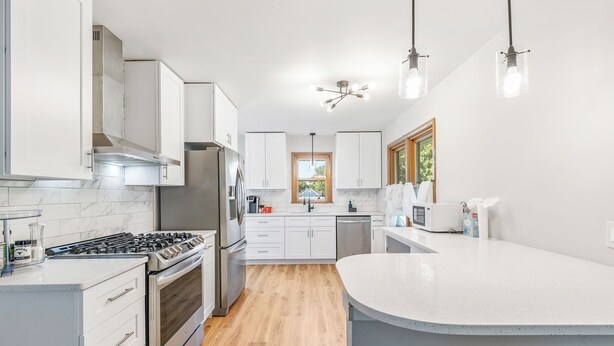 Une cuisine moderne avec des meubles blancs, un îlot central, des appareils en acier inoxydable et un plancher en bois.