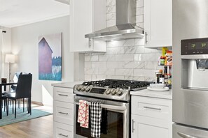 Een moderne keuken met een roestvrijstalen fornuis, oven en koelkast, een marmeren spatwand en een schilderij aan de muur.