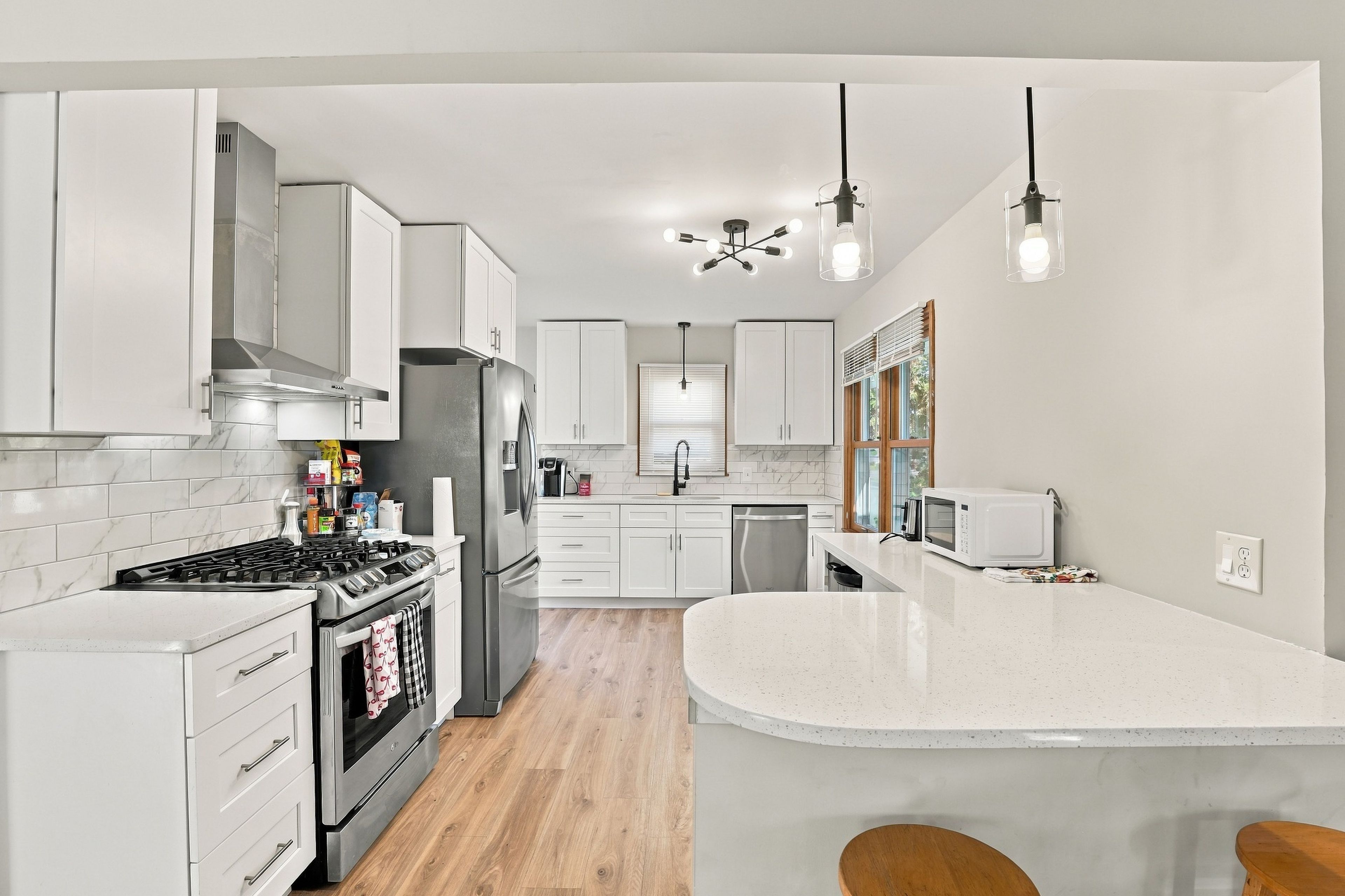Une cuisine moderne avec des meubles blancs, un îlot central, des appareils en acier inoxydable et des luminaires suspendus.