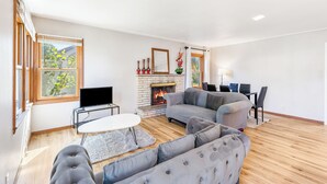 Un salon moderne avec une cheminée, des canapés gris, un téléviseur à écran plat et de grandes fenêtres.