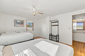 A bedroom with two beds, a ceiling fan, a wall-mounted mirror, and a window with blinds.