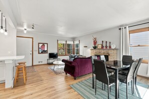 Een moderne woonkamer met een open haard, een eethoek met stoelen, een televisie en een keuken met een aanrecht en krukken.