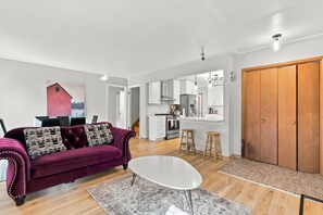 A modern living room with a sofa, a coffee table, and a kitchen in the background. - 4 bedroom HOUSE – 5 Minutes to MOA & AIRPORT (Minneapolis)