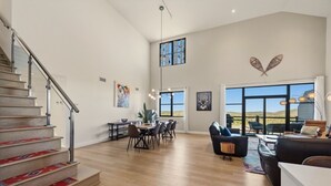 Een ruime woonkamer met een trap, een eettafel en een zithoek.