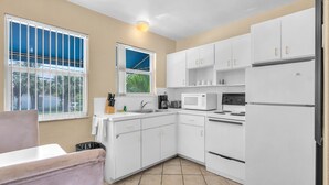 Una cocina con armarios blancos, microondas, estufa y lavaplatos.