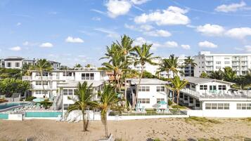 Um hotel à beira-mar com vários edifícios, piscina e palmeiras.