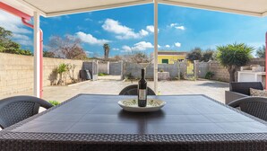 Un patio exterior con una mesa y sillas, una botella de vino y vistas a una zona residencial.