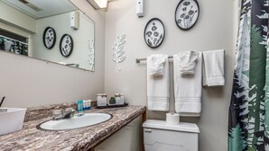A bathroom with a granite countertop, a white sink, a toilet, and a shower curtain with a leaf pattern.