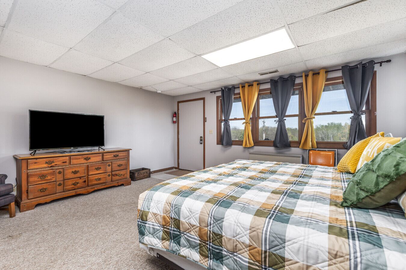 Une chambre à coucher avec un lit, une commode, un téléviseur et une fenêtre avec des rideaux.