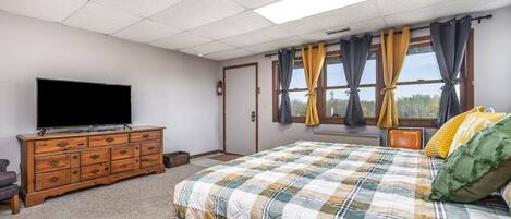 Une chambre à coucher avec un lit, une commode, un téléviseur et une fenêtre avec des rideaux.