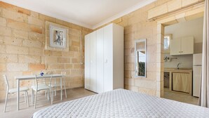 Un dormitorio con una cama, una mesa de comedor con sillas, un armario blanco y vistas a una cocina a través de una puerta abierta.