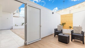 Una terrazza aperta con una porta scorrevole che dà su un balcone, mobili in vimini e un muro in legno.
