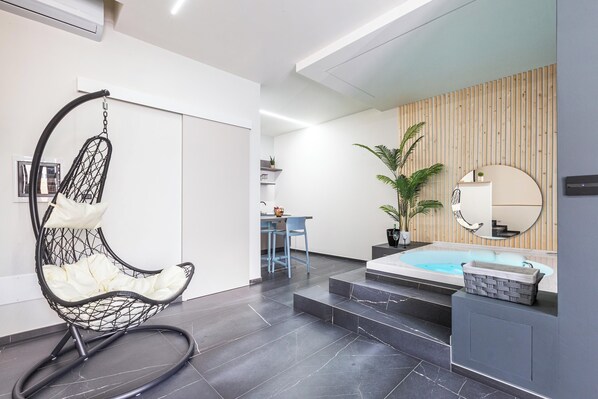 Un interior moderno con una silla colgante, un comedor, una cocina y un área de spa con jacuzzi.
