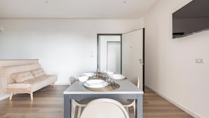 A modern dining area with a rectangular table set for six, surrounded by white chairs. A beige sofa is positioned in the background. - Mezzaluna Luxury Rooms - Mono Home (Mesagne)