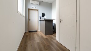 Un pasillo con suelo de madera, una puerta y un escritorio pequeño con un ordenador.