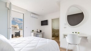 Un dormitorio moderno con una cama grande, un escritorio blanco, un espejo redondo y un televisor en la pared.