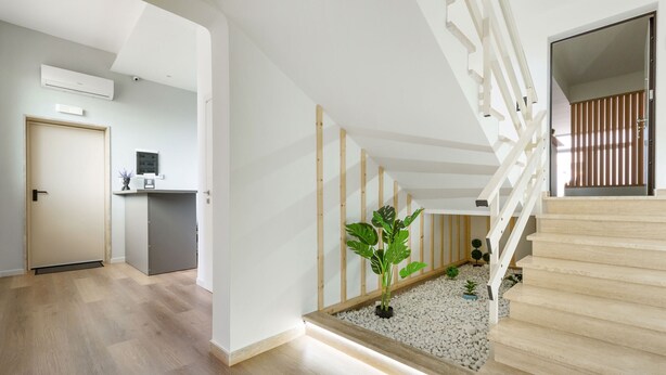 Un interior moderno con una escalera, suelo de madera y un pequeño jardín interior.