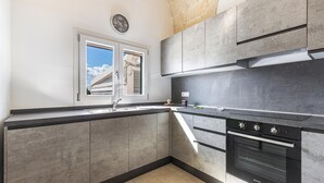 Una cocina moderna con armarios grises, un horno negro y una ventana con vistas a una casa.