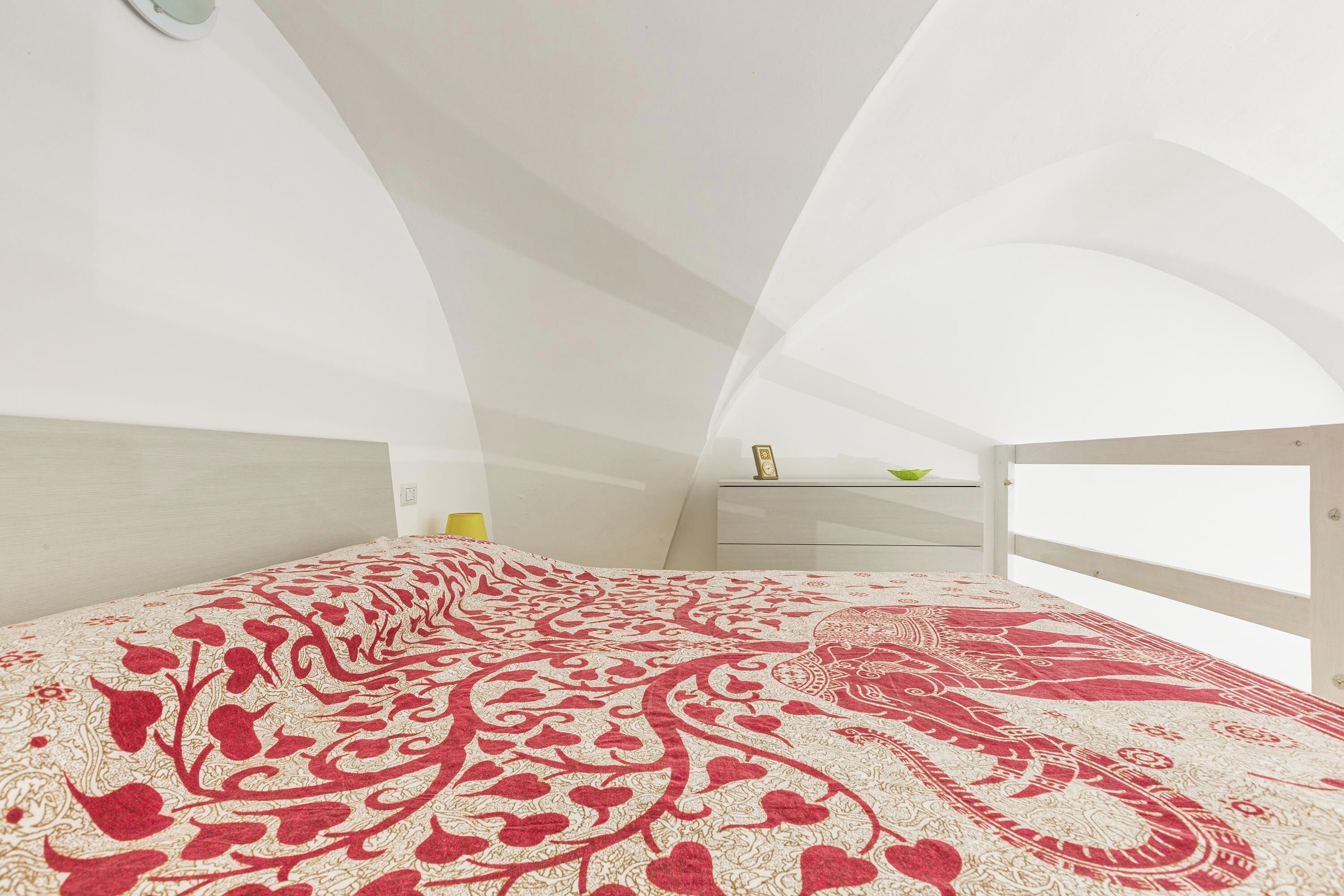 A bedroom with a large bed, white walls, and a curved ceiling.