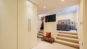 A bedroom with a bed, a TV, a bench, and a staircase. - Paddington 7-bed 13-guest Massive House W/patio (London)