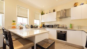 A modern kitchen with white cabinetry, a central island, and a built-in oven. - Paddington 7-bed 13-guest Massive House W/patio (London)