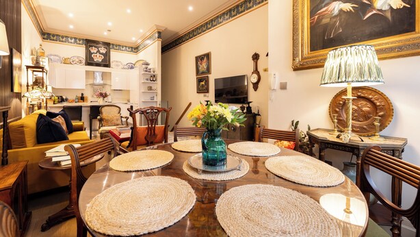 A dining area with a wooden table, woven placemats, and a vase with flowers. There are chairs around the table, and a painting is on the wall. - Paddington 7-bed 13-guest Massive House W/patio (London)