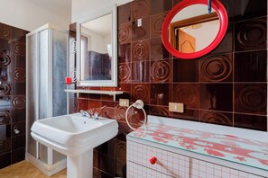 Un baño con un lavamanos blanco, un tocador con tapa de vidrio, una cabina de ducha y un espejo con marco rojo.