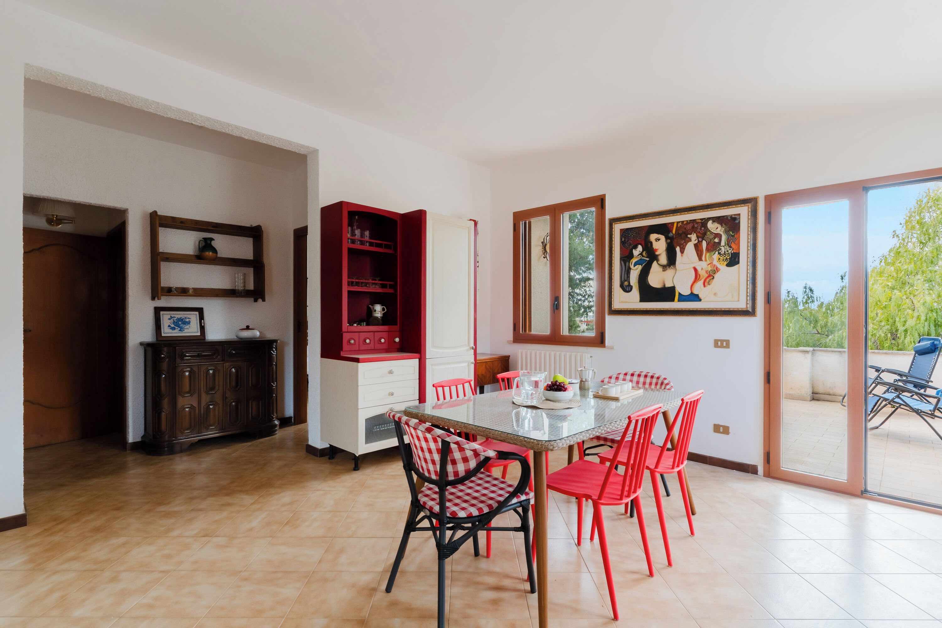 Un comedor con una mesa de vidrio, sillas a cuadros rojas y negras, un armario rojo y un cuadro en la pared.