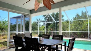 Un patio cubierto con una mesa y sillas, amplias ventanas y vistas a una piscina.