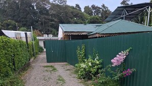 Un chemin de gravier mène à une zone délimitée par une clôture, surmontée d’une structure de toit en métal vert.