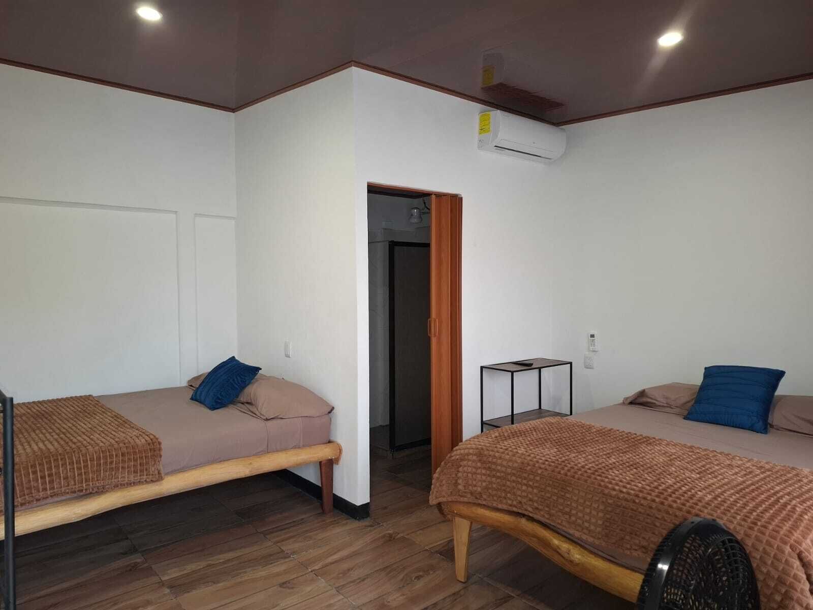 Una habitación con dos camas individuales, una mesita pequeña y un equipo de aire acondicionado.