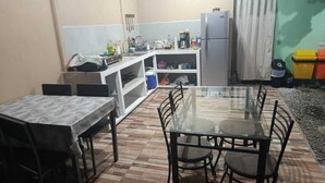 Une cuisine compacte comprenant une table et des chaises, un réfrigérateur et une petite étagère avec de la vaisselle et des ustensiles.