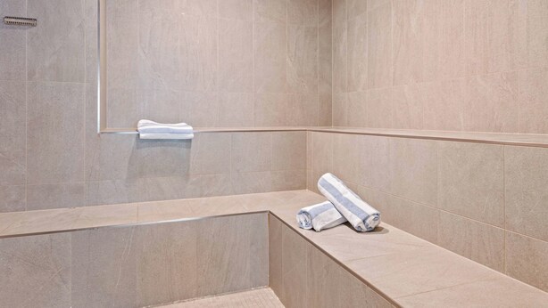 Une salle de bain moderne avec des carreaux de couleur beige, un banc intégré et un porte-serviettes.