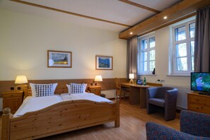 Ein Hotelzimmer mit einem hölzernen Bett, zwei Nachttischen mit Lampen, einem Schreibtisch mit Stuhl, einem Fernseher und zwei gerahmten Bildern an der Wand.