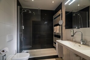 Ein modernes Badezimmer mit einer gläsernen Dusche, einer weißen Toilette, einem Waschbecken mit Spiegel und einem Handtuchhalter.