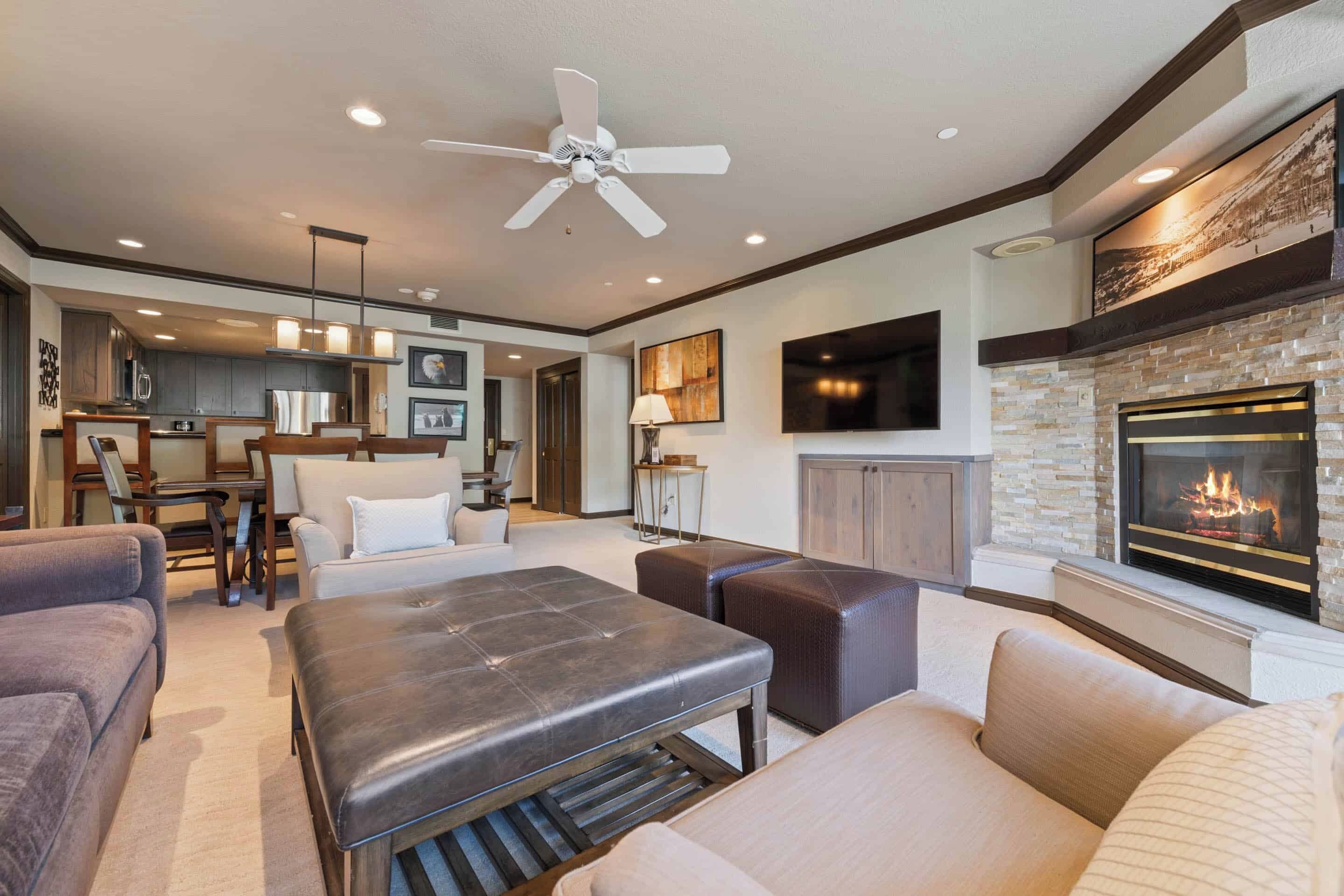 A modern living room with a fireplace, comfortable seating, and a kitchen area in the background.