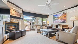 A spacious living room with a fireplace, comfortable seating, and large windows offering a view of the outdoors. - Saint James Place 111 (Beaver Creek)