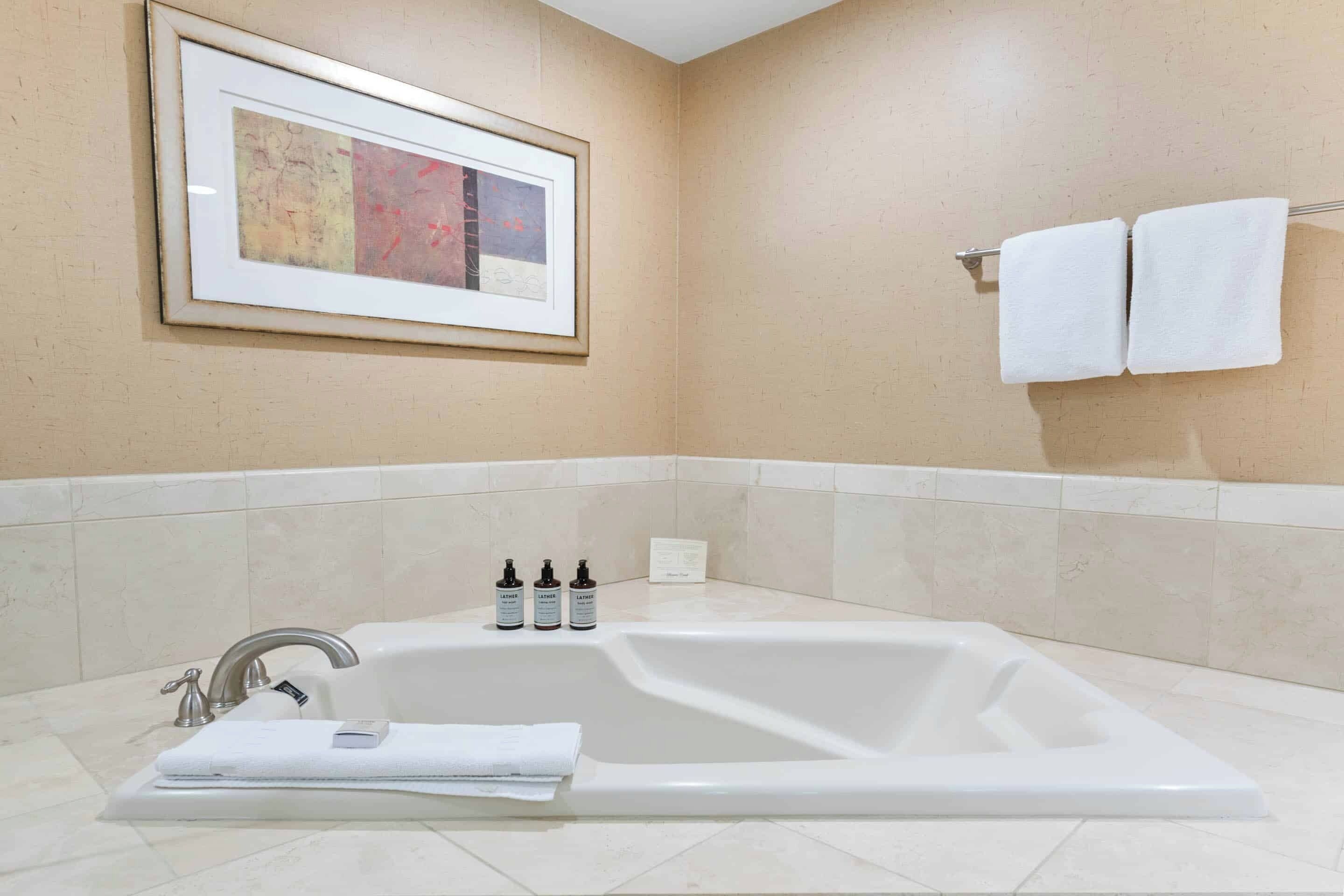 Ein modernes Badezimmer mit einer freistehenden Badewanne, einem gerahmten abstrakten Gemälde und einem Handtuchhalter mit zwei Handtüchern.