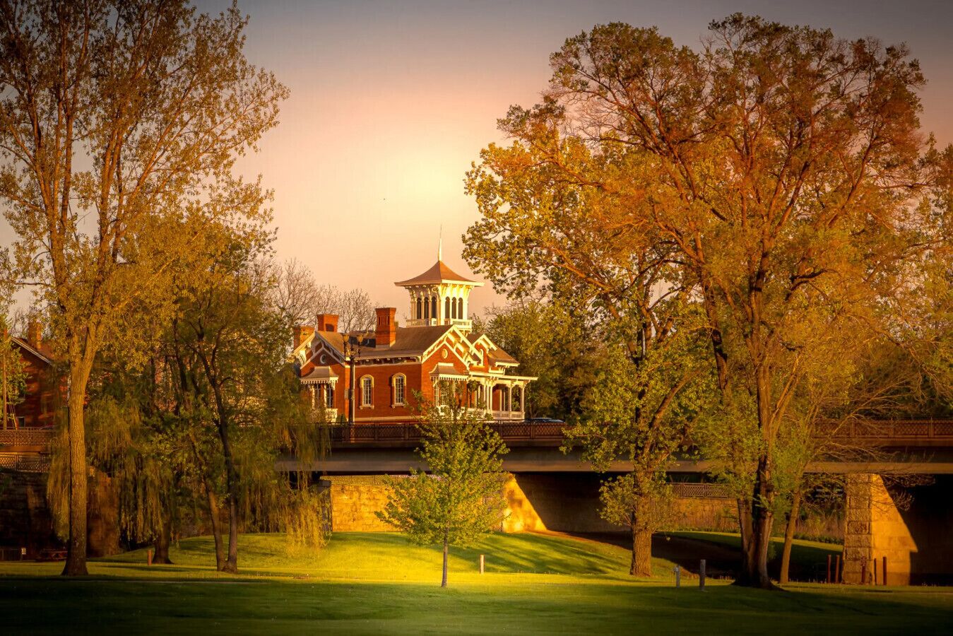 A large, historic building with a prominent tower and multiple chimneys, surrounded by lush trees and a well-maintained lawn.