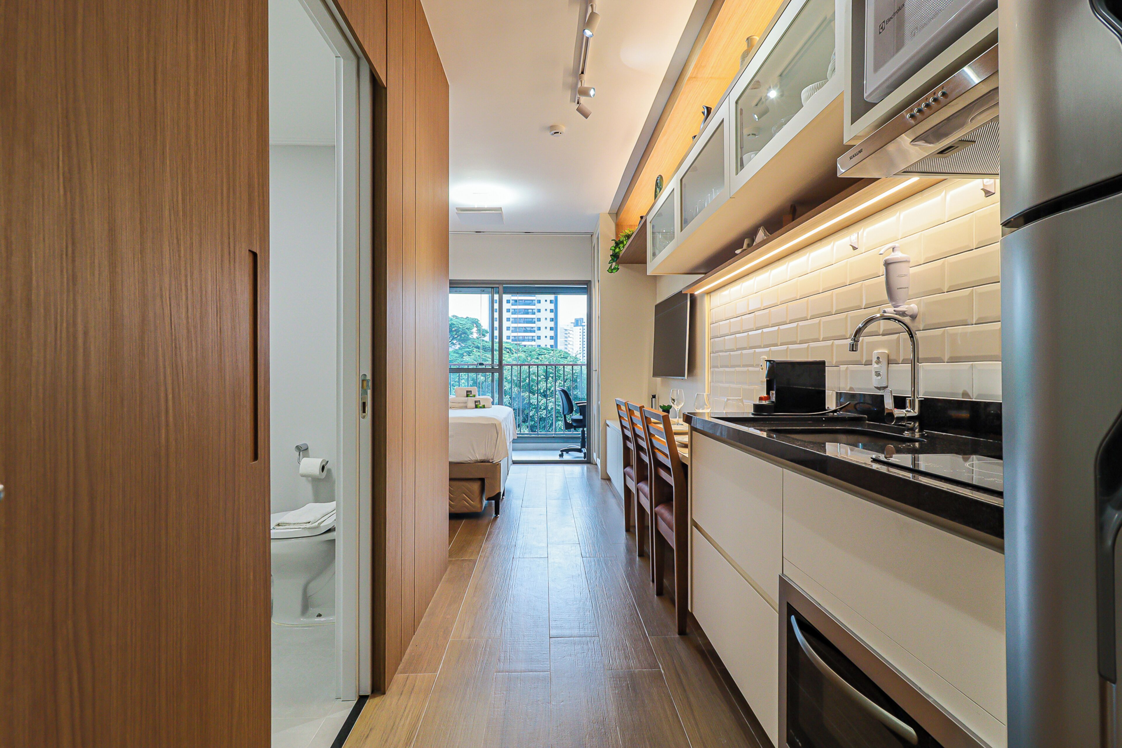 Una cocina moderna con suelo de madera, armarios blancos y electrodomésticos de acero inoxidable.