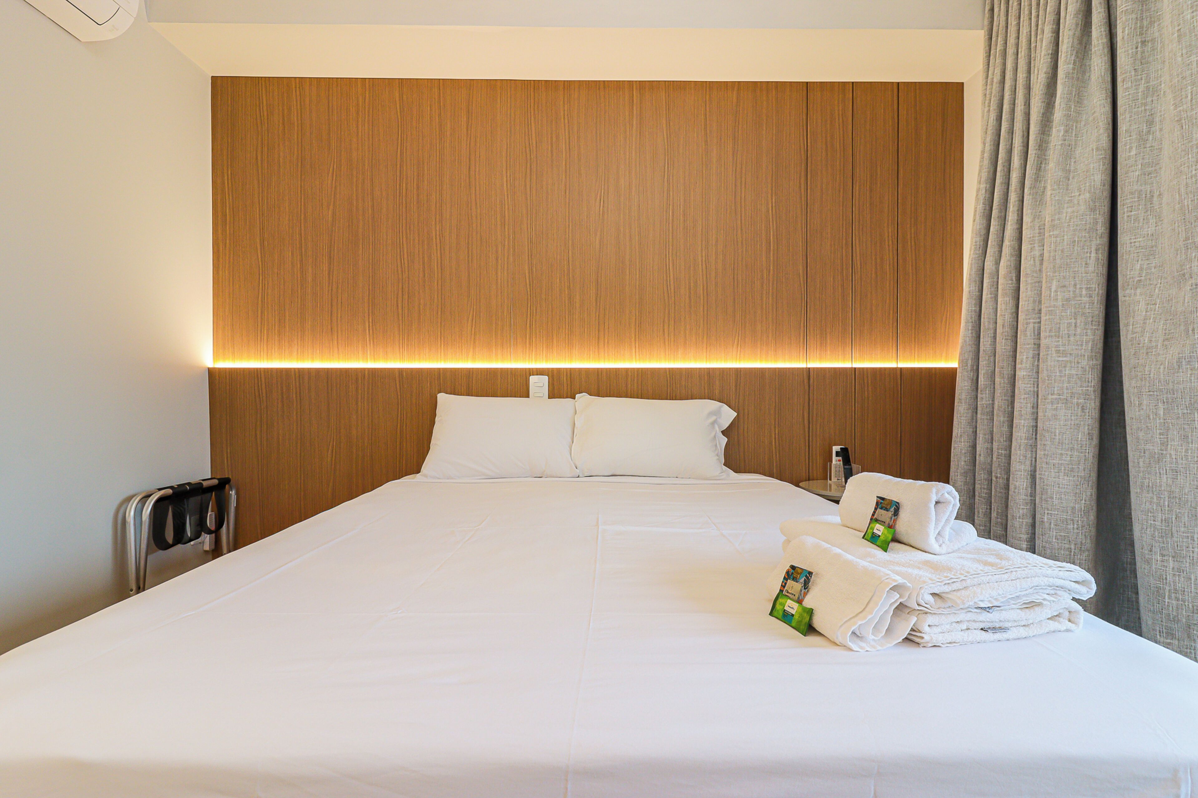 A hotel room with a large bed, wooden headboard, white linens, and neatly folded towels.