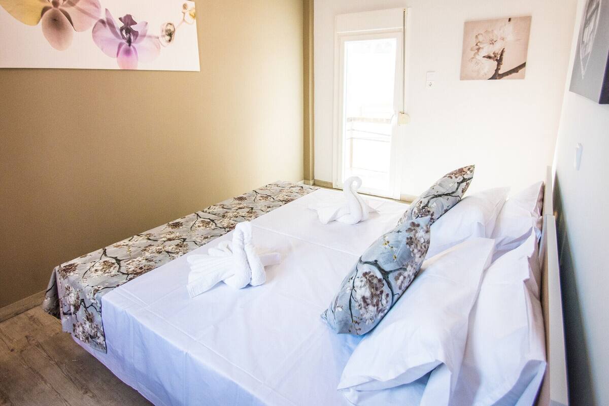 Ein Einzelbett mit blumigem Bettbezug, ein weißes, schwanenformiges Kopfkissen und ein passendes Kissen auf einem Wandregal.