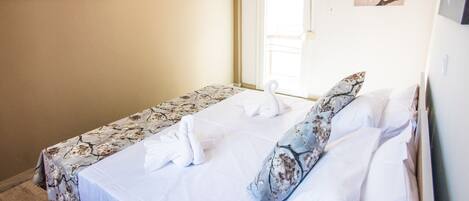 Un lit simple avec une literie à motifs floraux, un oreiller blanc en forme de cygne et un oreiller assorti posé sur une étagère fixée au mur.
