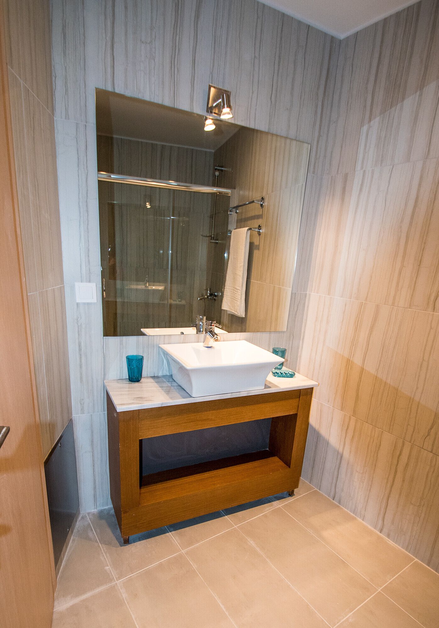 A modern bathroom with a large mirror, a white sink, and a wooden vanity.