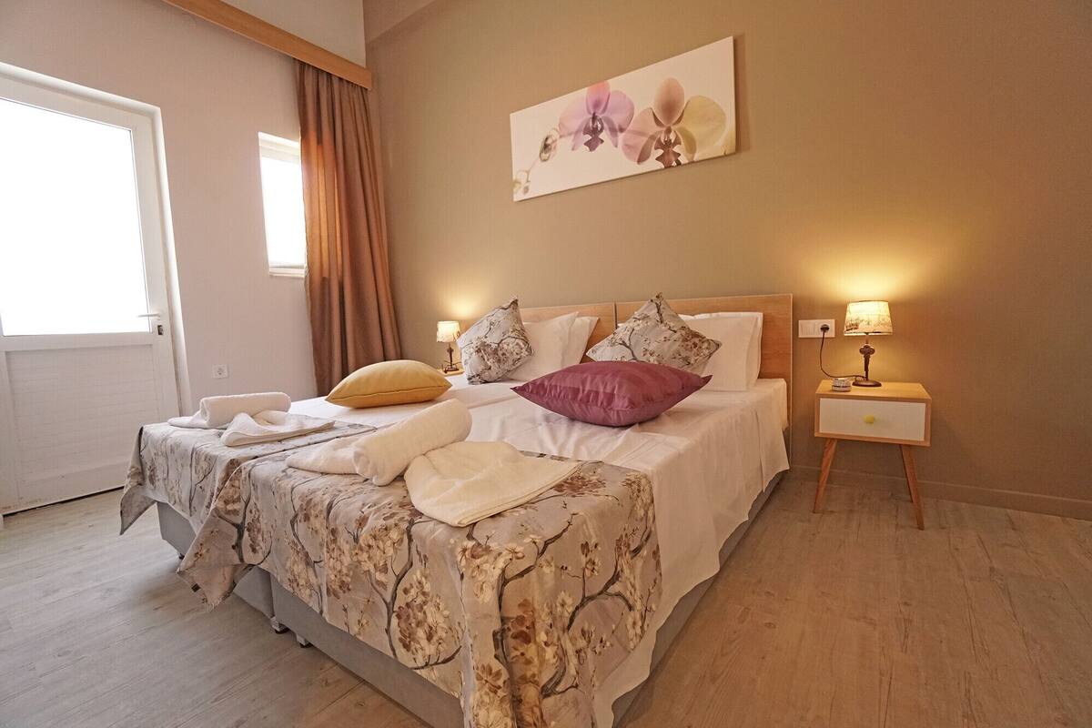 Ein Schlafzimmer mit Bett, Nachttisch, Lampe, einem Gemälde und einem Fenster mit Vorhängen.
