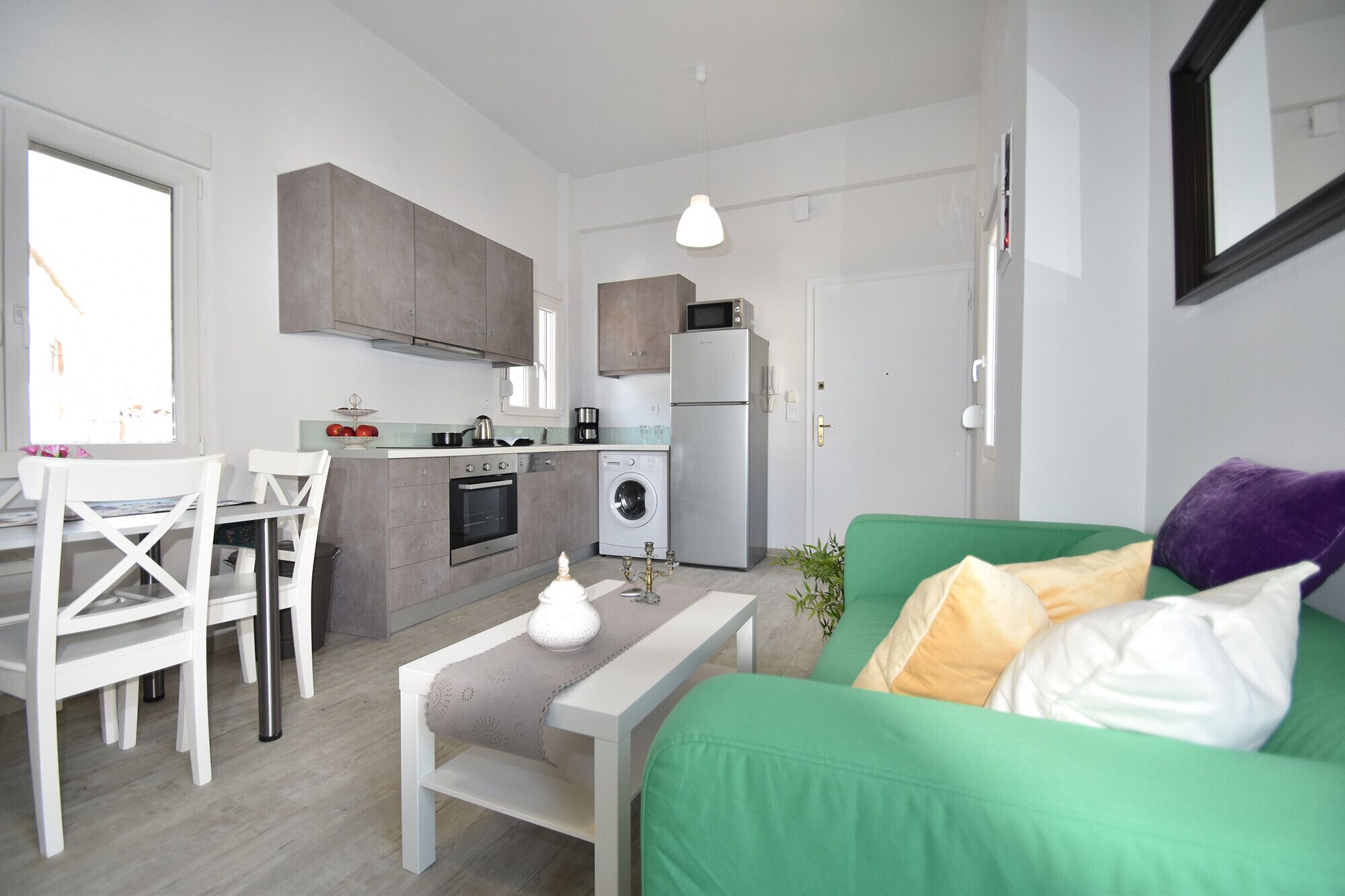 A compact living space with a kitchenette, a dining area, and a green sofa with cushions.